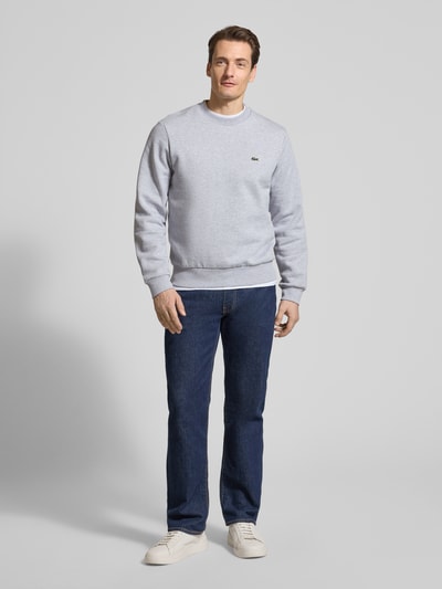 Męski model nosi Regular Fit Sweatshirt aus Baumwoll-Mix od Lacoste, efekt: jednolity kolor, naszywka z logo, okrągły dekolt, długi rękaw, prążkowane wykończenia, dzianina dresowa, mieszanka bawełny, ganzkörperansicht von vorne.