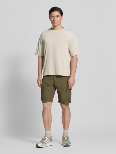 Mannelijk model draagt Bermudas met Cargozakken van camel active in olijfgroen, puur katoen, regular fit, steekzakken, labeldetail. Ganzkörperansicht von voren.