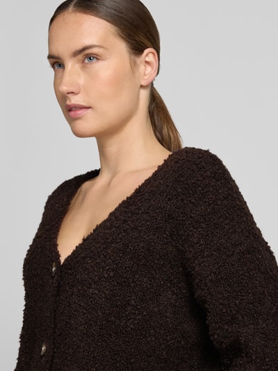 Vrouwenmodel draagt Relaxed Fit gebreid jack uit mix van wol en viscose Model 'Sofia' van ZABAIONE, donkerbruin, V-hals, knoopsluiting, fijngebreide textuur, dames, mix van wol en viscose, relaxed fit, lange mouwen, maat S/M ruglengte 62 cm, mouwlengte 45 cm, close-up bovenlichaam.