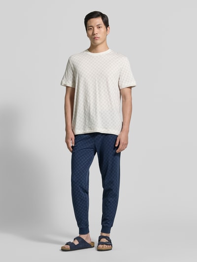 Männermodel trägt Sweatpants mit Logo-Muster und elastischem Bund von JOOP! Collection aus reiner Baumwolle im Regular-Fit, Ganzkörperansicht von vorne.