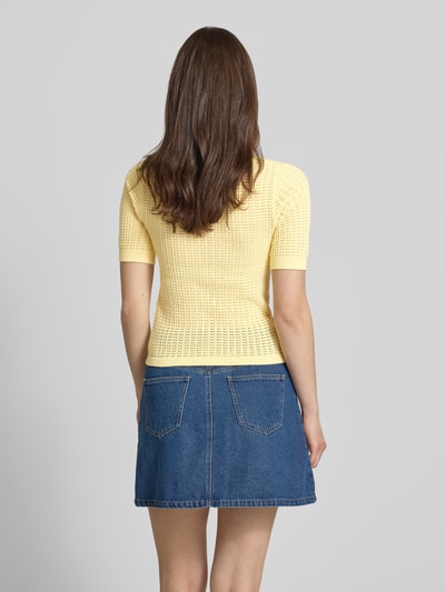 Frauenmodel trägt Slim Fit T-Shirt aus reiner Baumwolle Modell 'SCOUT' von Pieces in Optik: Unifarben, Struktur, Kurzarm, Denim-Minirock, Strick, sanft gelbe Farbe, gerippte Ärmel- und Rumpfabschluss, Semitransparente-Optik, Ganzkörperansicht Rückansicht.