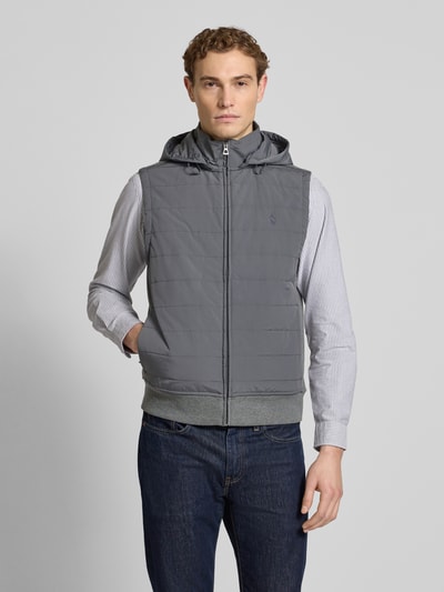 Męski model nosi Regular Fit Steppweste aus Baumwoll-Mix von Polo Ralph Lauren, szara, jednolita, krój regular fit, strukturalny wzór, logo, pikowana bawełna, dwie boczne kieszenie na zamek, ściągacz u dołu, z odpinanym kapturem i stójką, piqué, widok całej sylwetki z przodu.