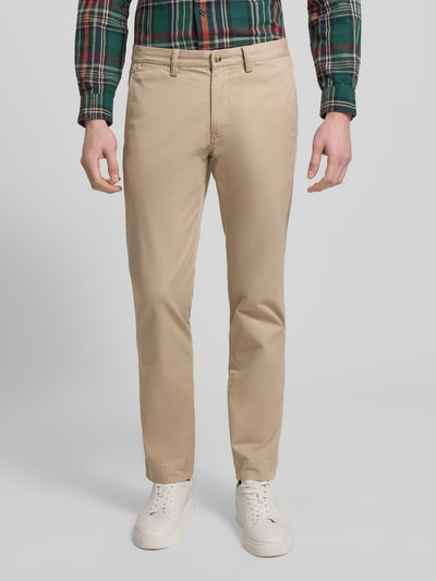 Męski model nosi Spodnie materiałowe z kieszeniami z tyłu od Polo Ralph Lauren, mieszanka bawełny i elastanu, krój slim fit, wpuszczane kieszenie, kieszenie z tyłu, zapięcie na guzik i zamek błyskawiczny, szerokość w rozmiarze 32/32: 43 cm, długość wewnętrzna nogawki w rozmiarze 32/32: 80 cm, beżowy kolor, gładka faktura, prosty krój, widok całej sylwetki z przodu.