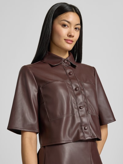 Frauenmodel trägt Cropped Bluse in Leder-Optik von VM by Vera Mont in Dunkelbraun mit Knopfleiste und Hemdblusenkragen, Nahaufnahme Oberkörper.