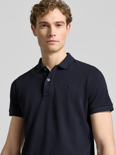 Männermodel trägt Slim Fit Poloshirt mit Logo-Stitching von Geox in Dunkelblau, Strukturmuster, reine Baumwolle, Nahaufnahme Oberkörper.