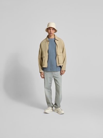 Männermodel trägt Regular Fit T-Shirt aus reiner Baumwolle von Closed in Blau, kombiniert mit heller Jacke und gestreifter Hose, Ganzkörperansicht von vorne.