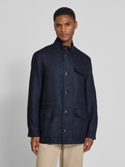 Męski model nosi Leinenjacke mit Stehkragen und Pattentaschen od bugatti z lnu, krój regular fit, stójka, listwa guzikowa, kieszenie z patką, ciemnoniebieski kolor, faktura lnu, długość tyłu w rozmiarze 50: 74 cm, szerokość ramion w rozmiarze 50: 46 cm, szerokość klatki piersiowej w rozmiarze 50: 55 cm, długość rękawów w rozmiarze 50: 64 cm, całkowity widok z przodu