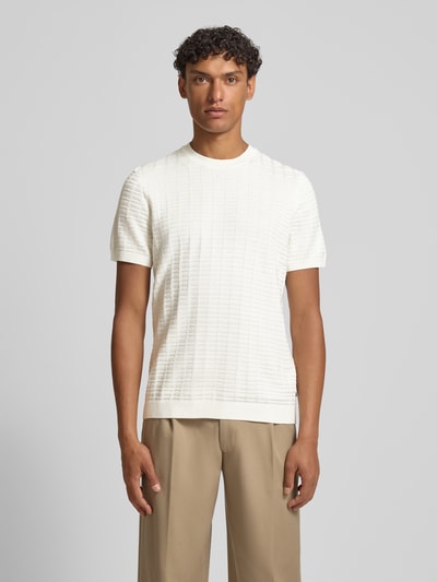 Männermodel trägt T-Shirt mit Label-Detail Modell 'Theor' von JOOP!, weiß, gerader Schnitt, feine Textur, Ganzkörperansicht von vorne.