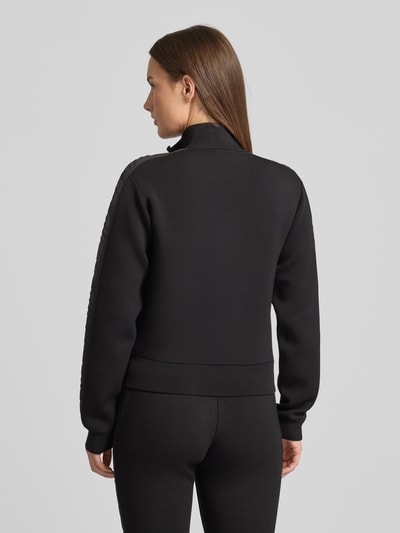 Frauenmodel trägt Regular Fit Sweatjacke aus Viskose-Mix von Guess Activewear in Schwarz mit Stehkragen und Logo, Ganzkörperansicht Rückansicht.