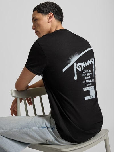 Männermodel trägt Regular Fit T-Shirt aus reiner Baumwolle von Tommy Jeans in Schwarz, Optik: Unifarben, Label-Print, Ganzkörperansicht Rückansicht.