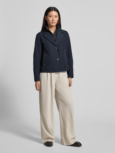 Modelka kobieca ma na sobie kurtkę 'Jacke im 2-in-1-Look' od Amber & June, krój regular fit, efekt 2 w 1, kołnierz z połami, listwa guzikowa, detal z logo, długość tyłu w rozmiarze 36: 65 cm, szerokość ramion w rozmiarze 36: 42 cm, szerokość klatki piersiowej w rozmiarze 36: 51 cm, długość rękawów w rozmiarze 36: 63 cm, kolor granatowy, prosta tkanina, przód całopostaciowy