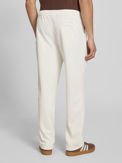 Männermodel trägt Trackpants mit Längsnähten Modell 'Motus' von Pegador aus Material-Mix mit Baumwoll-Anteil, Relaxed-Fit, Ganzkörperansicht Rückansicht.