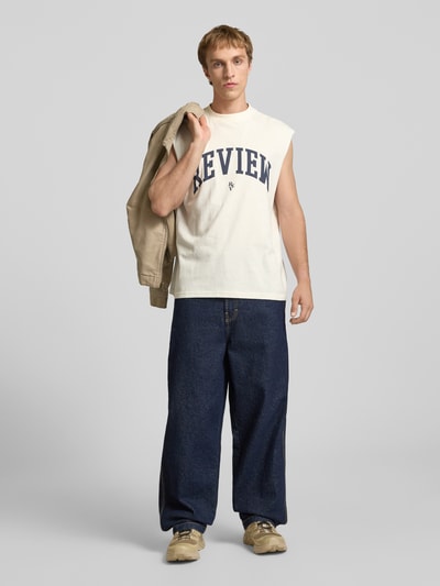 Männermodel trägt Tanktop mit Logo-Print von REVIEW in Beige aus Reine Baumwolle, Gerader-Schnitt, Rundhalsausschnitt, Rückenlänge 68 cm, Ganzkörperansicht von vorne.