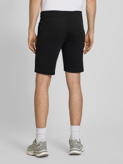 Männermodel trägt Shorts mit Logo-Print Modell 'GORDON' von Jack & Jones aus schwarzem Baumwoll-Mix im Relaxed-Fit, Ganzkörperansicht Rückansicht.