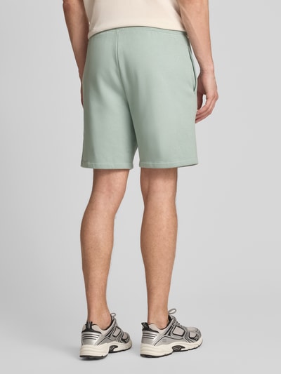 Männermodel trägt Sweatshorts mit Logo und elastischem Bund von GAP aus mintgrünem Baumwoll-Mix mit Eingrifftaschen, Regular-Fit, Ganzkörperansicht Rückansicht.
