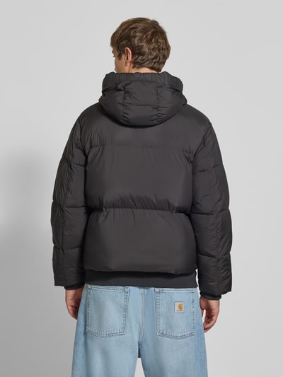 Männermodel trägt Regular Fit Pufferjacke mit Kapuze von Tommy Jeans in Schwarz, Stepp-Optik, Ganzkörperansicht Rückansicht.