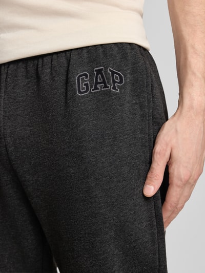Mężczyzna nosi spodnie dresowe 'Sweatpants mit Logo und elastischem Bund' od GAP z mieszanki bawełny, krój regular fit, logo, elastyczny pas, długość wewnętrzna nogawki 78 cm w rozmiarze M, zbliżenie na biodra