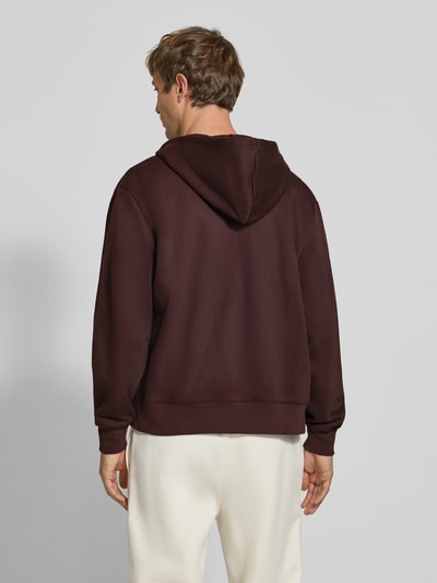 Männermodel trägt Sweatjacke mit Label-Stitching und Känguru-Tasche von Champion, brauner Baumwoll-Mix, Rückansicht, Ganzkörperansicht.