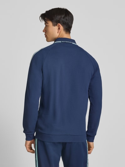 Männermodel trägt Regular Fit Trainingsjacke mit Deutschland Logo von adidas Sportswear in Dunkelblau, Kontraststreifen, Rückansicht.