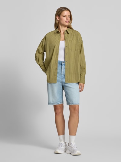 Frauenmodel trägt Relaxed Fit Hemdbluse aus reiner Baumwolle Modell 'JAMIE' von JJXX mit feinen Streifen, helle Farben, Ganzkörperansicht von vorne, Damen Hemdbluse, Hemdblusenkragen, langärmlig, aufgesetzte Brusttasche, durchgehende Knopfleiste, überschnittene Schultern, Rückenlänge 77 cm, Ärmellänge 56 cm.