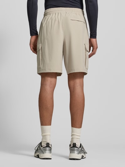 Männermodel trägt beige Straight Fit Shorts mit Cargo-Taschen Modell 'Vibe' von Under Armour, elastischer Bund, Ganzkörperansicht Rückansicht.