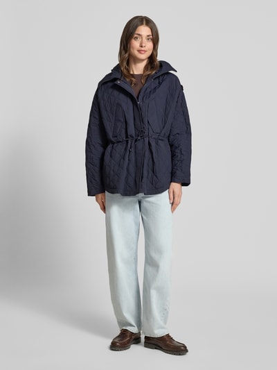 Frauenmodel trägt Relaxed Fit Jacke in Stepp-Optik Modell 'Texel' von Peuterey in Dunkelblau, mit Stehkragen, Pattentaschen und Tunnelzug, strukturierte Oberfläche, Ganzkörperansicht von vorne.