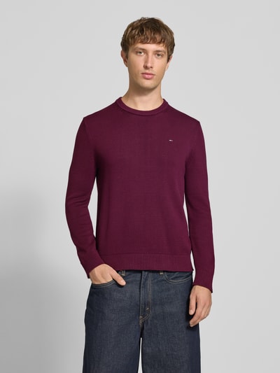 Männermodel trägt Slim Fit Pullover aus reiner Baumwolle von Tommy Jeans in Unifarbe Beere mit Strickstruktur, Nahaufnahme Oberkörper.