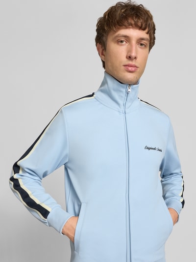 Männermodel trägt hellblaue Sweatjacke mit Stehkragen Modell 'COTEDAZUR' von Jack & Jones, Slim-Fit, Label-Stitching und Reißverschluss, Ganzkörperansicht von vorne. Herren Sweatjacke, Rückenlänge bei Größe M 70 cm, Ärmellänge 65 cm.