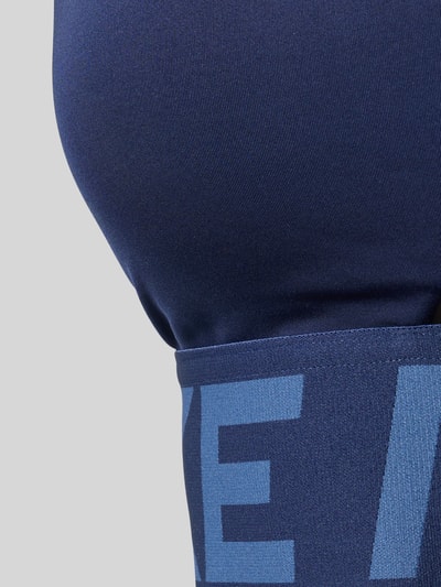 Frauenmodel trägt Bustier mit Label-Details und Cut-Out von NIKE TRAINING in Dunkelblau, glatte Textur, Label groß sichtbar, Detailaufnahme.