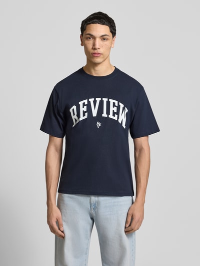 Männermodel trägt T-Shirt mit Label-Print und Rundhalsausschnitt von REVIEW aus reiner Baumwolle in Dunkelblau, Ganzkörperansicht von vorne.