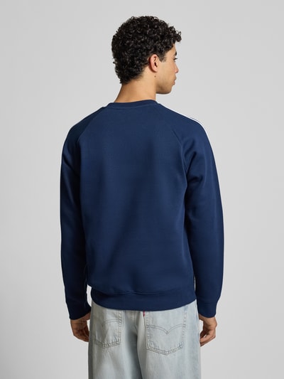 Męski model nosi bluzę Sweatshirt mit Label-Stitching od adidas Originals, mieszanka bawełny i elastanu, luźny krój, prążkowane wykończenia, okrągły dekolt, długość tyłu 68 cm, długość rękawa 58 cm, widok całej sylwetki z tyłu.