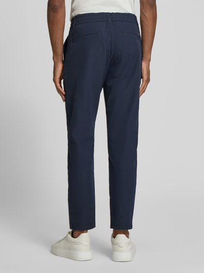 Männermodel trägt Tapered Chino mit Tunnelzug von BOSS Orange in Dunkelblau, unifarben, mit Gürtelschlaufen und Taschen, Ganzkörperansicht Rückansicht.
