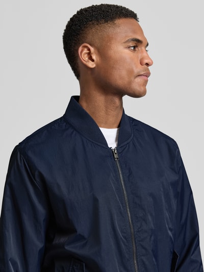 Männermodel trägt Regular Fit Bomberjacke mit Stehkragen von s.Oliver RED LABEL in Dunkelblau, glatte Struktur, Nahaufnahme Oberkörper.