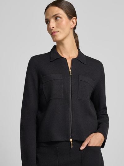 Modelka nosi Regular Fit kardigan rozpinany z czystej wiskozy od Christian Berg Woman, wykładany kołnierz, luźny krój, brustasza, zamek błyskawiczny dwustronny, długość tyłu w rozmiarze S 53 cm, długość rękawów w rozmiarze S 61 cm, kolor czarny, gładka tekstura, zbliżenie na górną część sylwetki, przód.