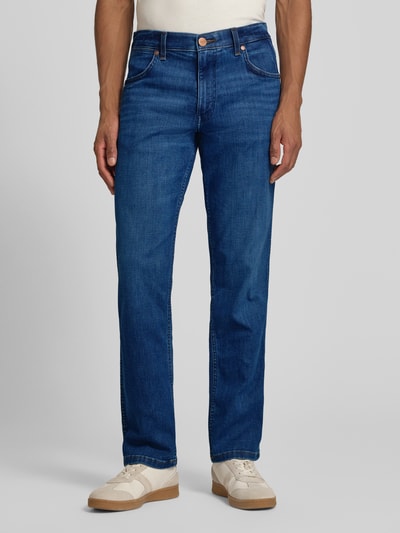 Männermodel trägt Straight Fit Jeans im 5-Pocket-Design Modell 'Greensboro' von Wrangler aus Baumwoll-Mix mit Stretch-Anteil, Gerader-Schnitt, Knopf-Reißverschluss, mittleres Blau, glatte Textur, Ganzkörperansicht von vorne.