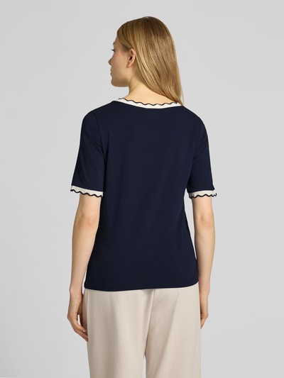 Modelka nosi T-Shirt mit Rundhalsausschnitt und Wellensaum od More & More, bawełna z elastanem, krój regular fit, długość pleców w rozmiarze 36: 57 cm, granatowy z białymi wykończeniami, widok całej sylwetki od tyłu.