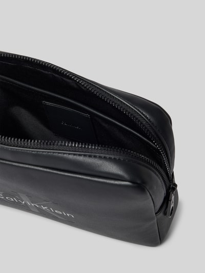 Produktfoto, schwarze Henkeltasche mit Label-Prägung von CK Calvin Klein für Herren, glatte Oberfläche, silberner Zip, Innenfach sichtbar.