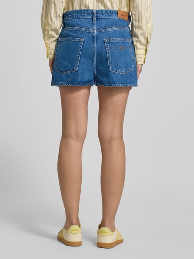 Frauenmodel trägt Regular Fit Jeansshorts aus reiner Baumwolle von Lacoste in klassischem Denim-Blau mit Logo-Patch und 5-Pocket-Design, Ganzkörperansicht Rückansicht.