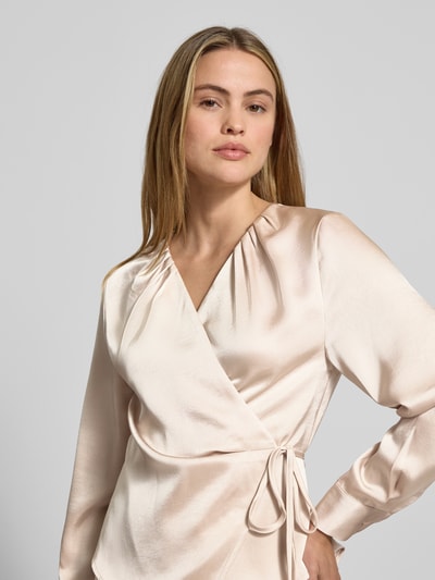 Frauenmodel trägt Wickelbluse aus Satin Modell 'Caprina' von Neo Noir, cremefarben, taillierter Schnitt, V-Ausschnitt, Nahaufnahme Oberkörper.