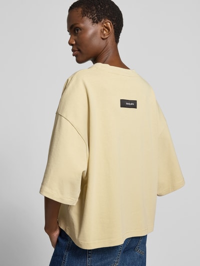 Frauenmodel trägt T-Shirt mit Rundhalsausschnitt von black palms aus reiner Baumwolle im Relaxed-Fit, Halbarm, helles Beige, Rückenlänge 55 cm, Ganzkörperansicht Rückansicht.