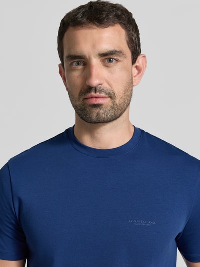 Męski model nosi Extra Slim Fit T-Shirt mit Rundhalsausschnitt von Armani Exchange w kolorze niebieskim, nadruk z logo, Nahaufnahme Oberkörper.