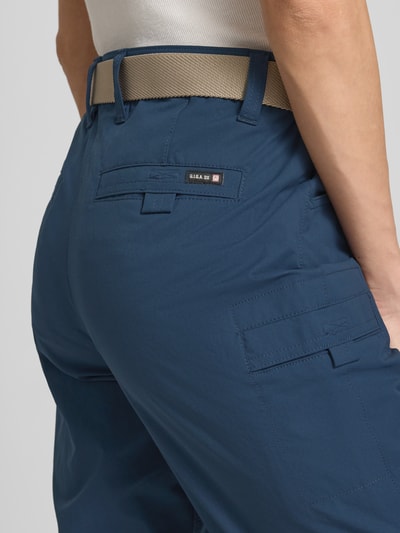 Frauenmodel trägt Bermudas mit Pattentaschen und Saum mit fixiertem Aufschlag von G.I.G.A. DX, blaue Farbe, Label-Patch, Nahaufnahme Rückansicht, HYDROCOOL EFFEKT, Knopf-Reißverschluss, Gürtel, seitliche Eingrifftaschen, Gesäßtaschen, Bundweite Größe 36: 38 cm, Innenbeinlänge Größe 36: 41 cm.