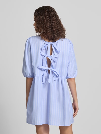 Frauenmodel trägt Relaxed Fit Blusenkleid mit Streifenmuster Modell 'CLARA TESSA' von Only, hellblau-weiß, Schleifen, Ballonärmel, recyceltes Material, Ganzkörperansicht Rückansicht.