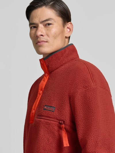 Männermodel trägt Fleecepullover mit Label-Patch Modell 'Helvetia™ II' von Columbia in Rot, Struktur Fleece, Nahaufnahme Oberkörper. Rückenlänge 70 cm, Ärmellänge 62 cm, Stehkragen, kurze Knopfleiste, Brusttasche mit Reißverschluss.