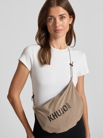 Frauenmodel trägt weiße T-Shirt von khujo, helle Crossbody-Bag mit Logo-Aufdruck, glatter Stoff, Nahaufnahme Oberkörper.