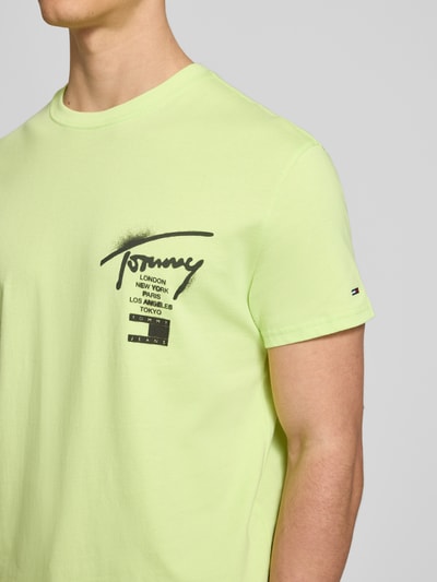 Męski model nosi Regular Fit T-Shirt aus reiner Baumwolle von Tommy Jeans, jasny jednolity kolor, czarny nadruk z logo, jersey, krótki rękaw, okrągły dekolt, zbliżenie na górną część ciała