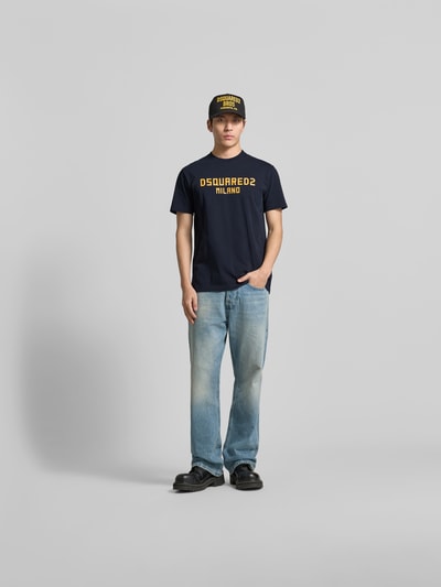 Männermodel trägt Cool Fit T-Shirt aus reiner Baumwolle von Dsquared2 in Dunkelblau mit gelbem Statement-Print, Ganzkörperansicht von vorne.