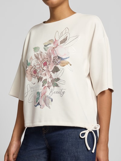 Frauenmodel trägt Relaxed Fit T-Shirt mit Statement-Print von Christian Berg Woman, floraler Print in Pastell, elastischer Material-Mix, Nahaufnahme Oberkörper.