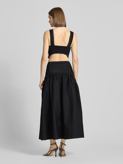 Frauenmodel trägt Maxikleid mit rückseitigem Cut Out Modell 'ALINA' von Topshop aus schwarzem Baumwoll-Mix mit Stretch-Anteil, taillierter Schnitt, Häkelspitze, rückseitige Smok-Details, glatte und leicht strukturierte Stofftextur, Ganzkörperansicht Rückansicht.