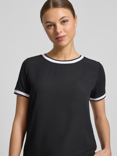 Modelka nosi Regular Fit T-Shirt aus Viskose-Mix von More & More, czarny T-shirt z białym obszyciem, elastyczny materiał, krój regular fit, okrągły dekolt, krótki rękaw, długość tyłu w rozmiarze 36: 57 cm, zbliżenie na górną część ciała z przodu.